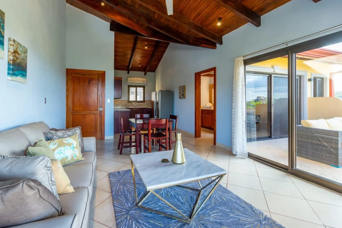 A bright living and dining area with a coffee table beside sliding glass doors.