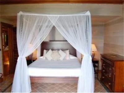 Un dormitorio con una cama con dosel cubierta de cortinas blancas y transparentes.