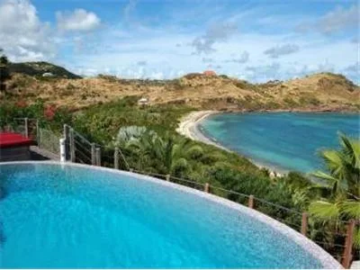 Una piscina curva tiene vistas a una bahía turquesa y colinas secas.