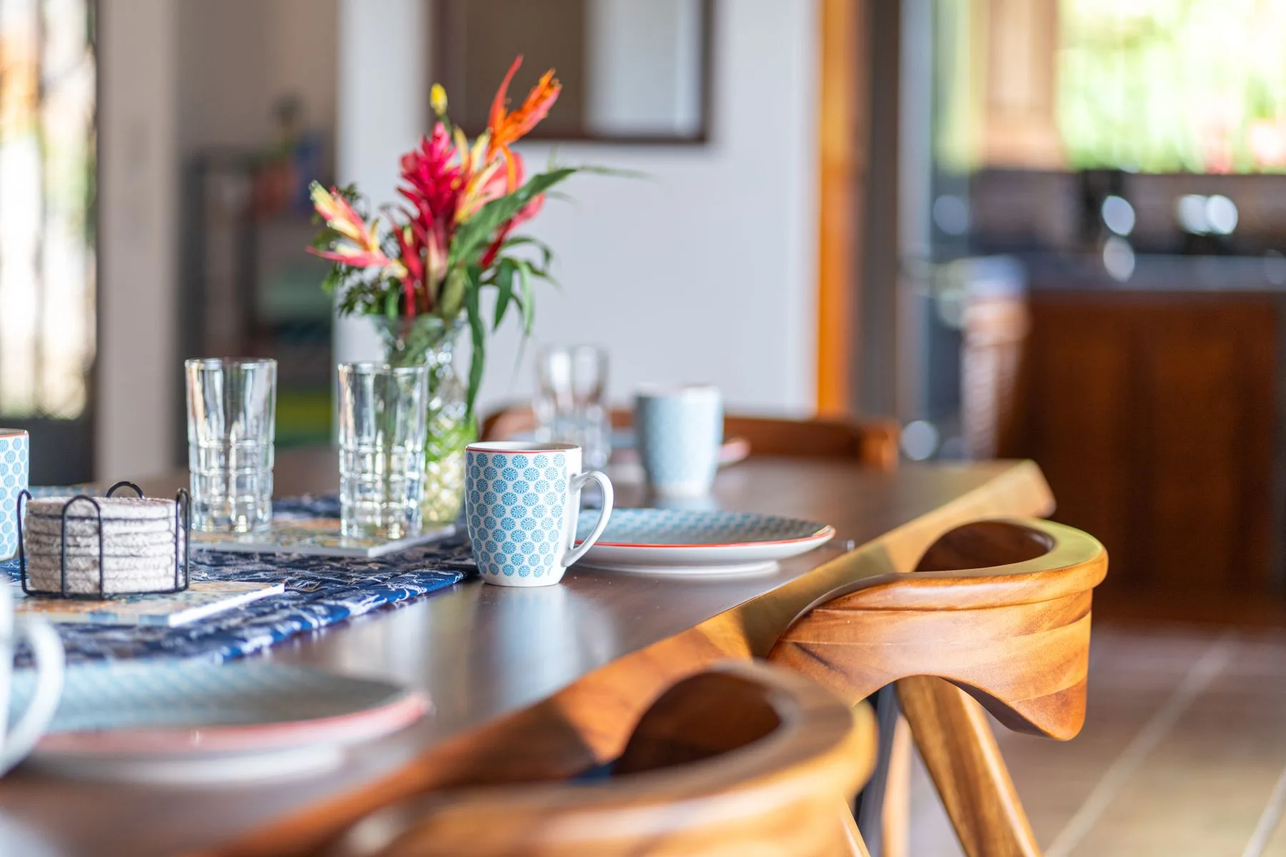 A dining table is set with cups, glasses, and a colorful flower arrangement.
