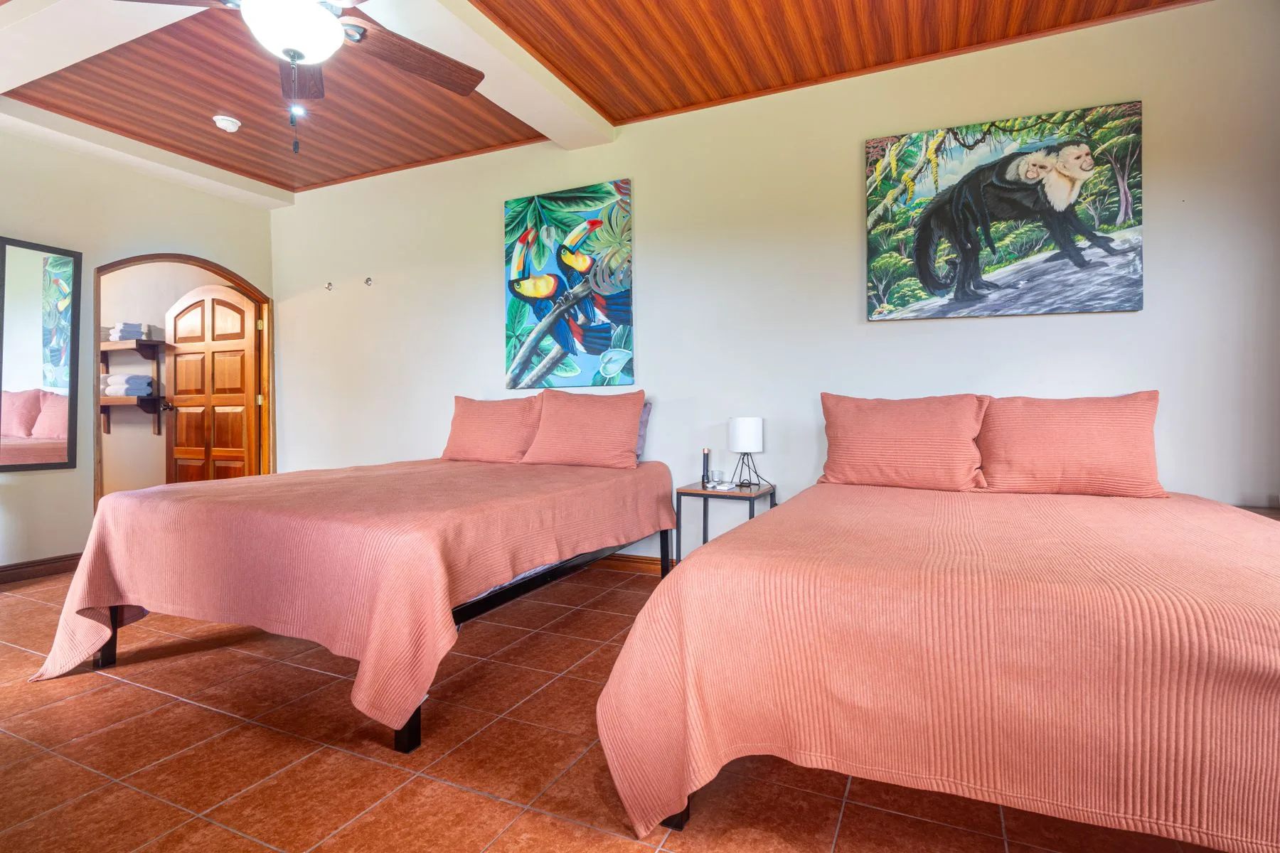A bedroom with two beds dressed in coral-colored bedding and tropical artwork.
