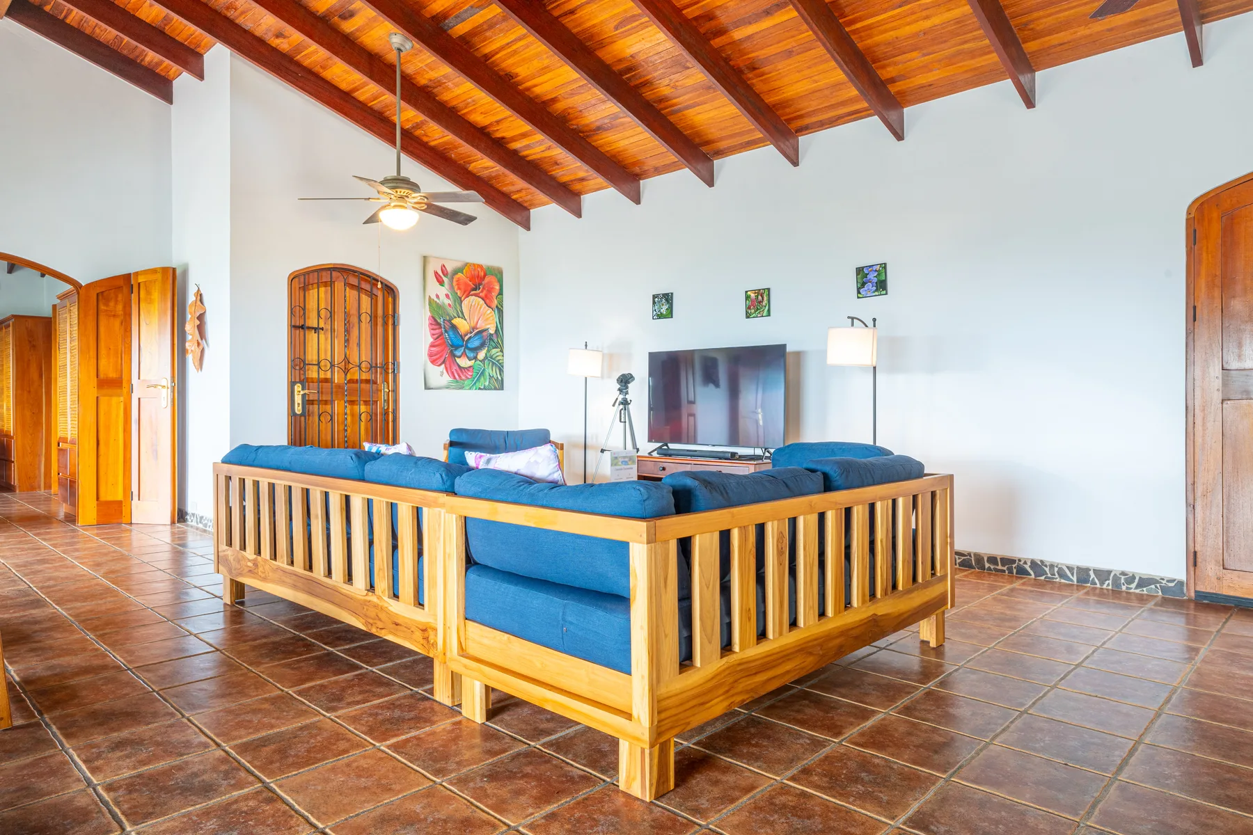 A living room with blue seating arranged around a television beneath a wooden-beam ceiling.
