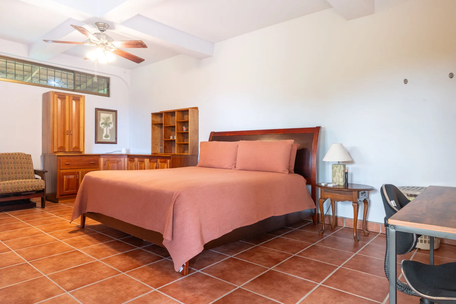 A bedroom with a large bed, wooden furniture, and a tiled floor.
