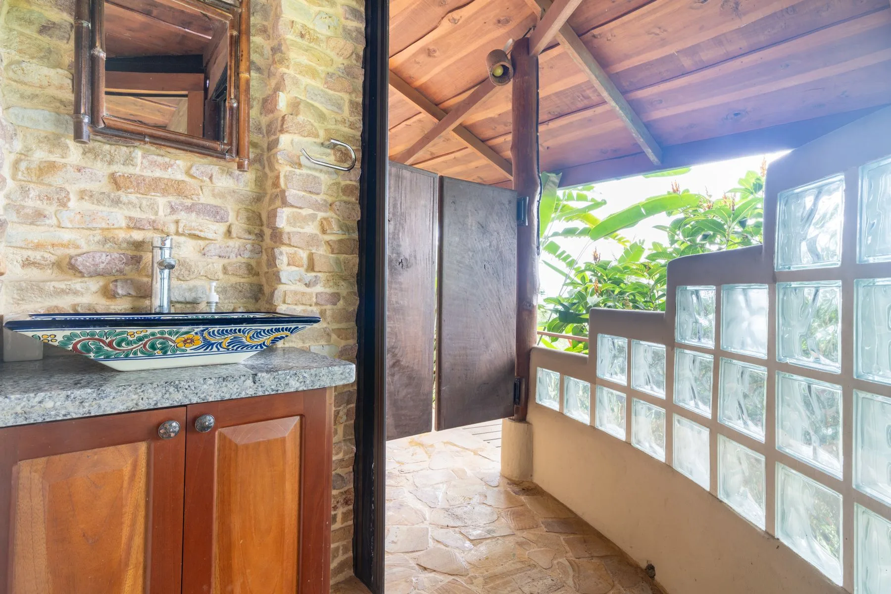 A rustic bathroom vanity opens onto a covered walkway with glass-block walls.