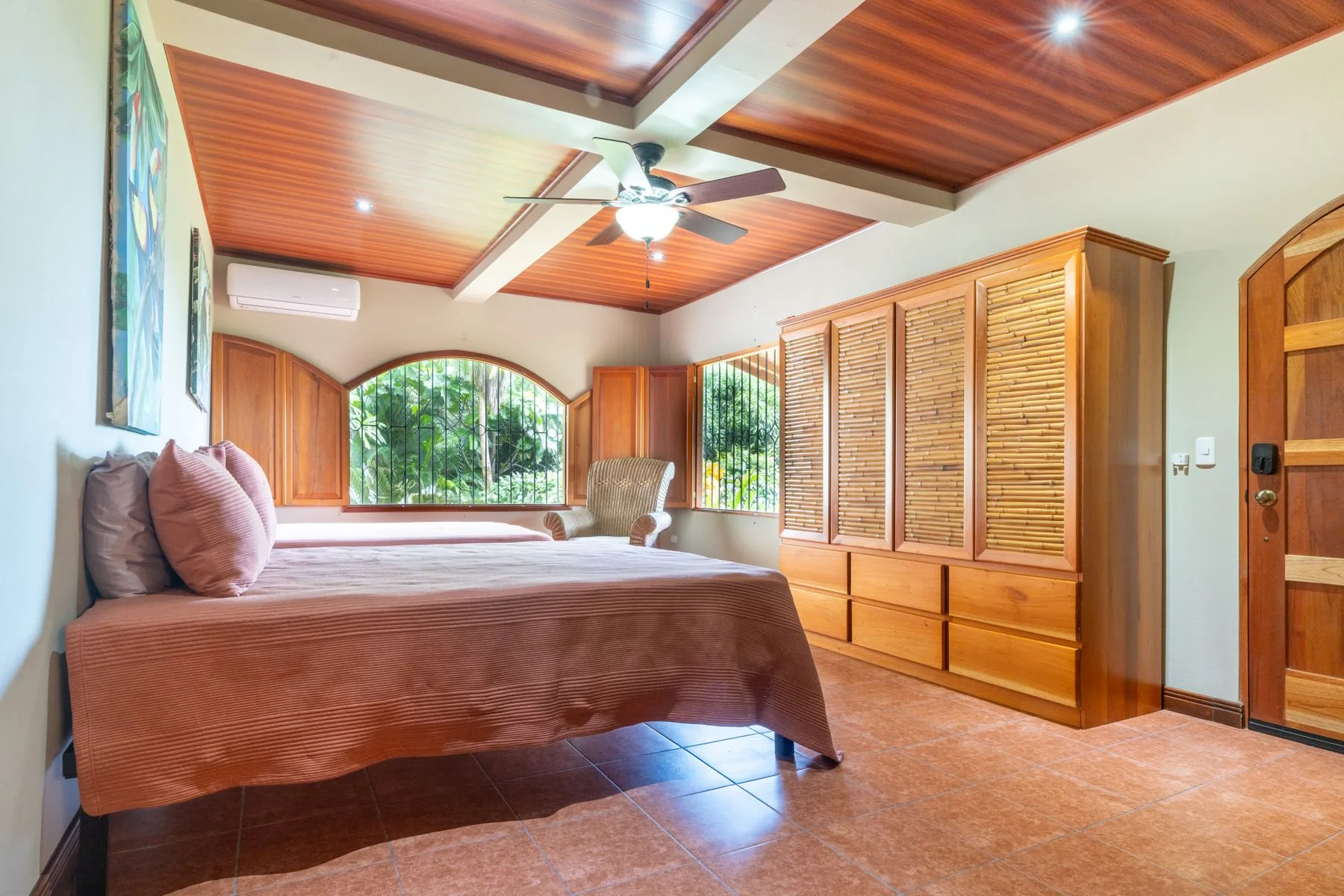 A bedroom with a bed, wooden cabinetry, and large arched windows.