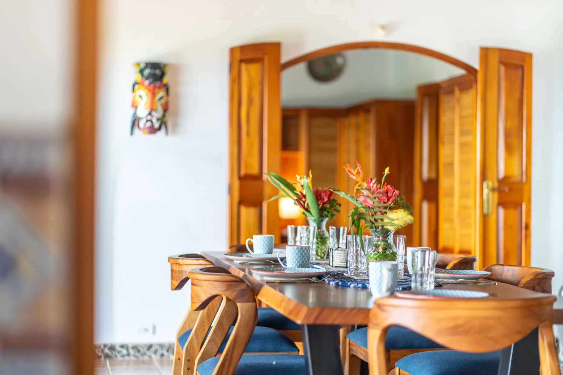 A dining table is set with dishes and flowers in front of wooden doors.
