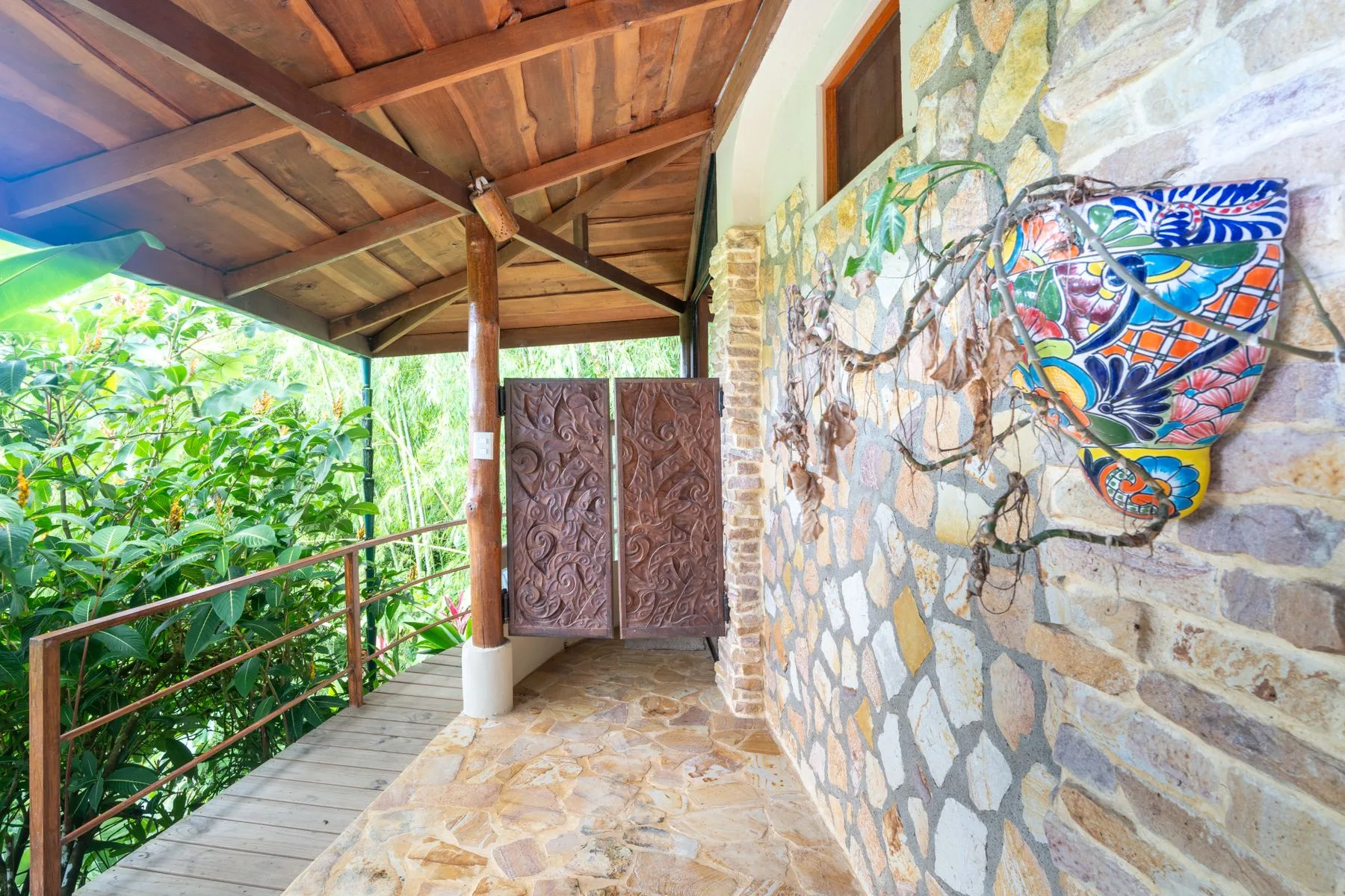 A covered stone walkway has a wooden railing and a colorful wall decoration.