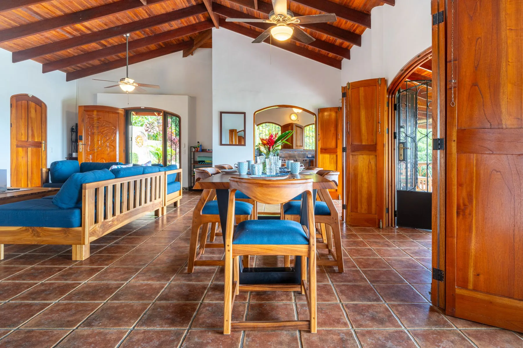 A dining and living area with a wooden table, blue seating, and a beamed ceiling.