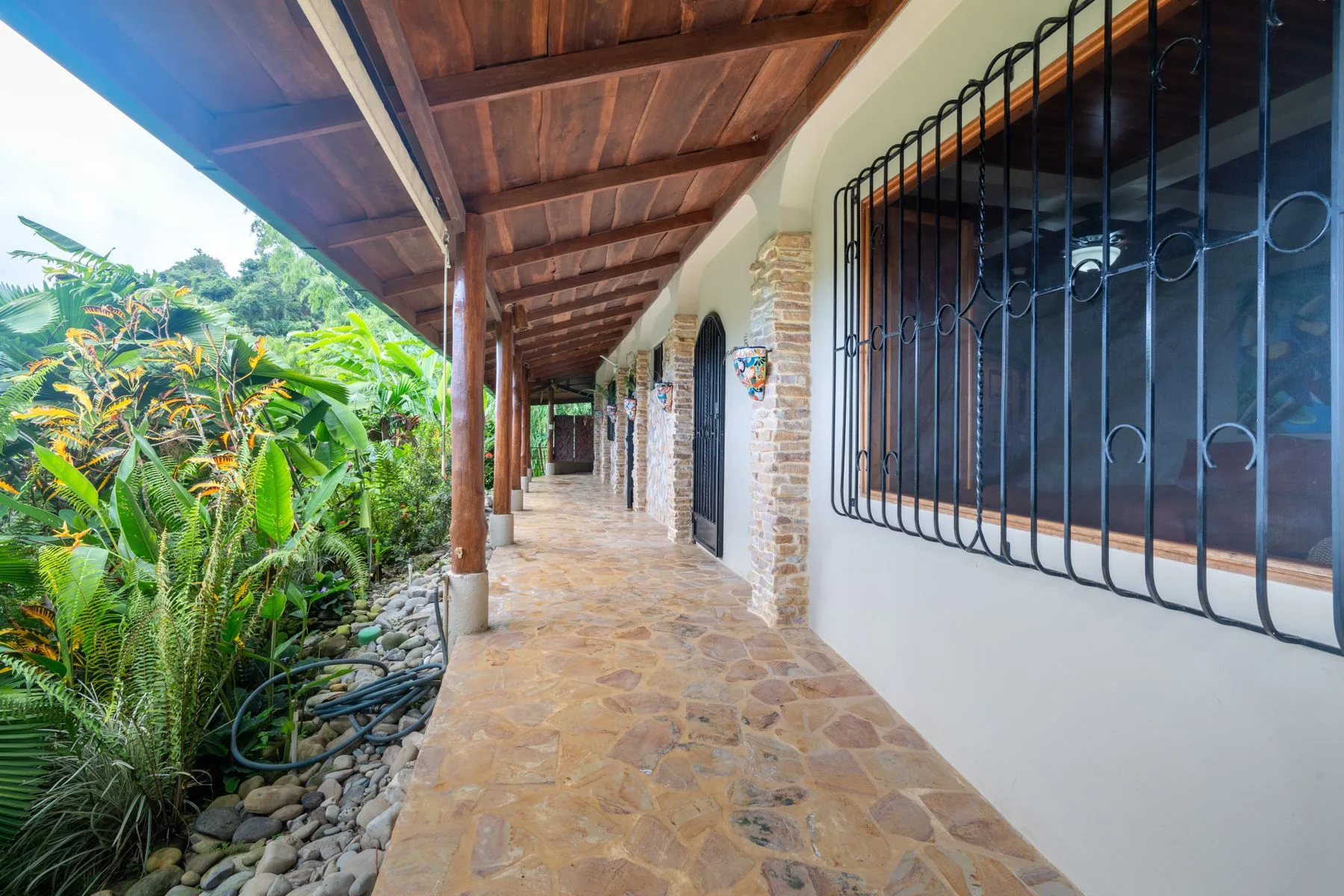 A covered stone walkway runs beside barred windows and dense tropical greenery.