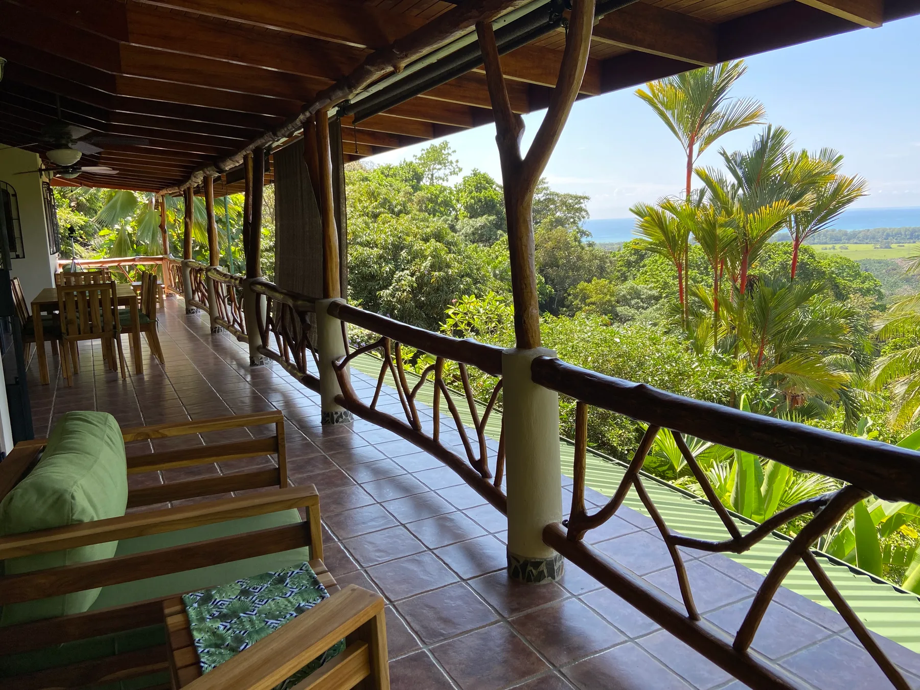 A covered outdoor veranda with seating overlooks lush trees and distant water.