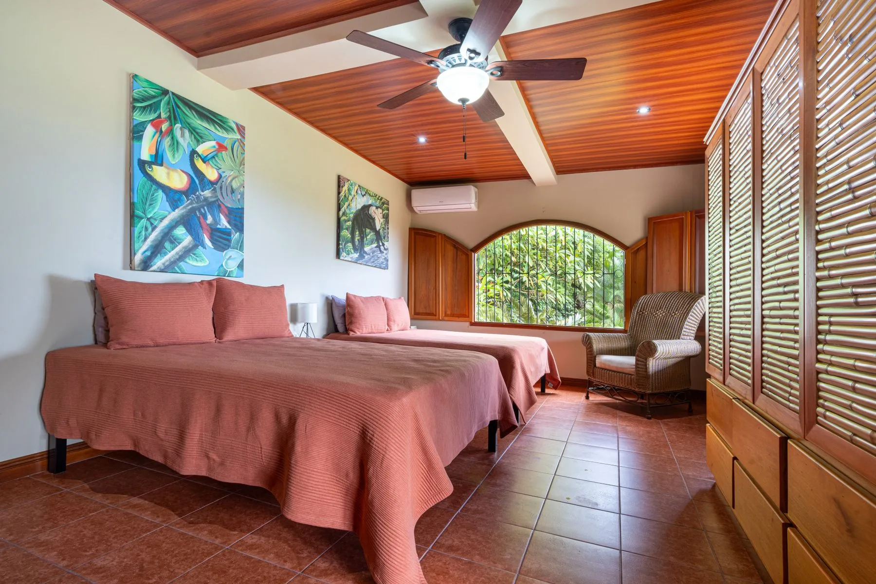 A bedroom with two beds, a ceiling fan, and a large arched window.