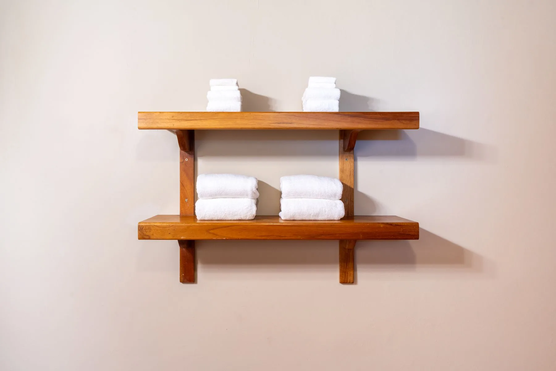 A wall-mounted wooden shelf holds neatly folded white towels.