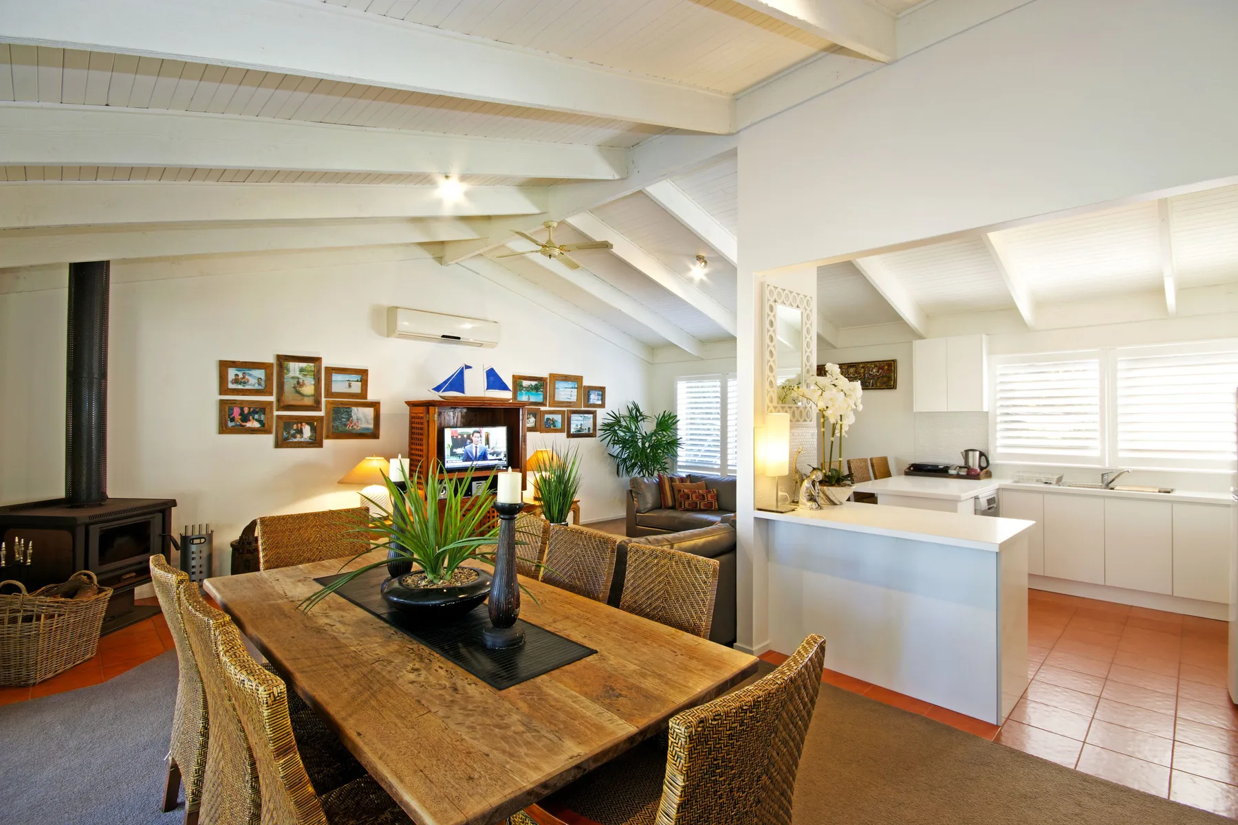 A dining area beside an open kitchen, with a wooden table and woven seating.