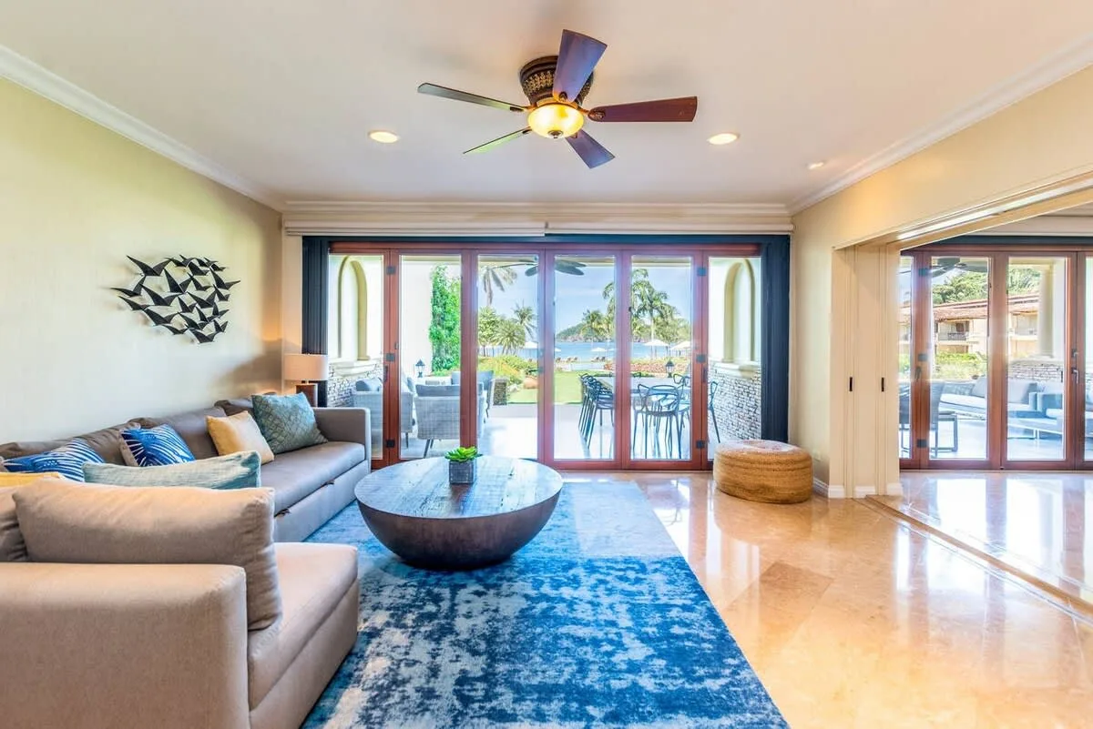 A bright living room with seating, a coffee table, and glass doors opening to a patio.