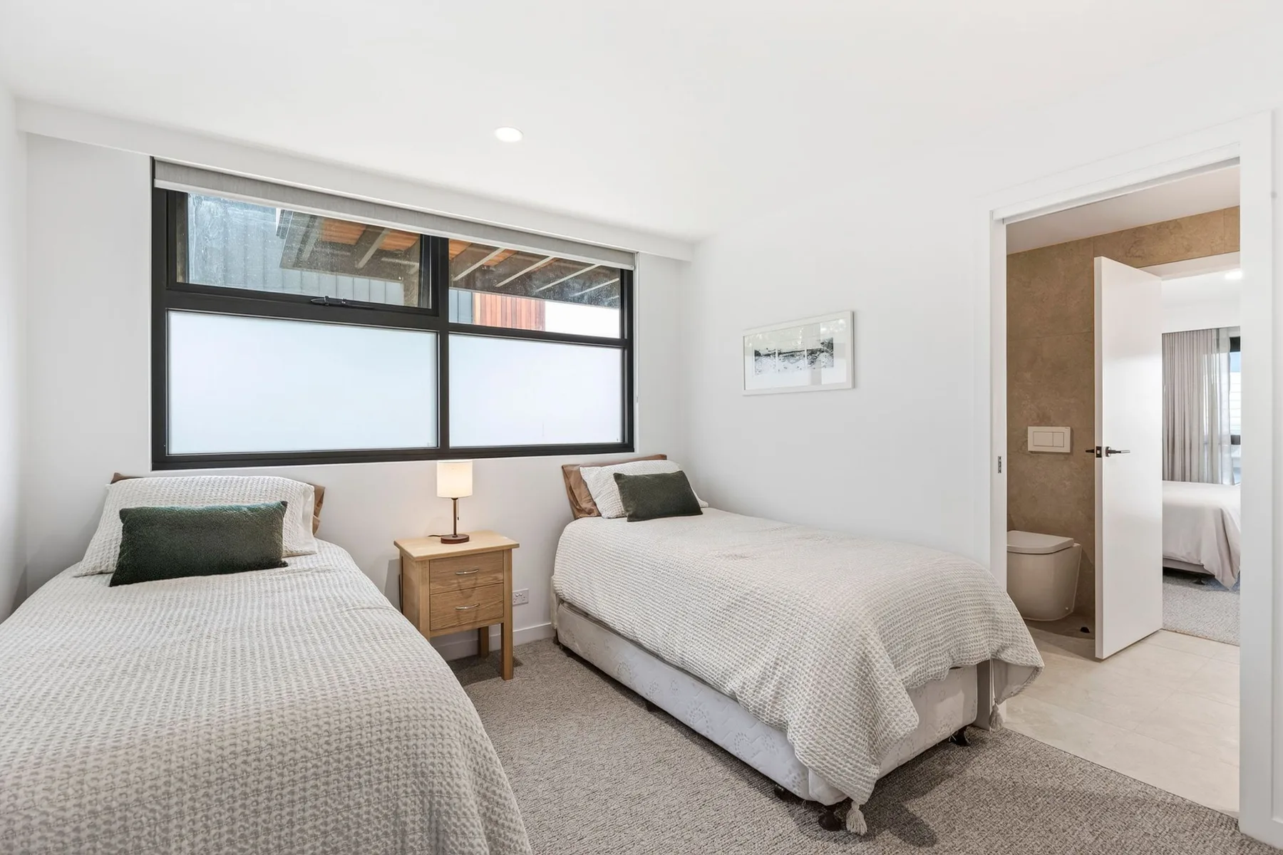 Un dormitorio luminoso con dos camas junto a una ventana grande.