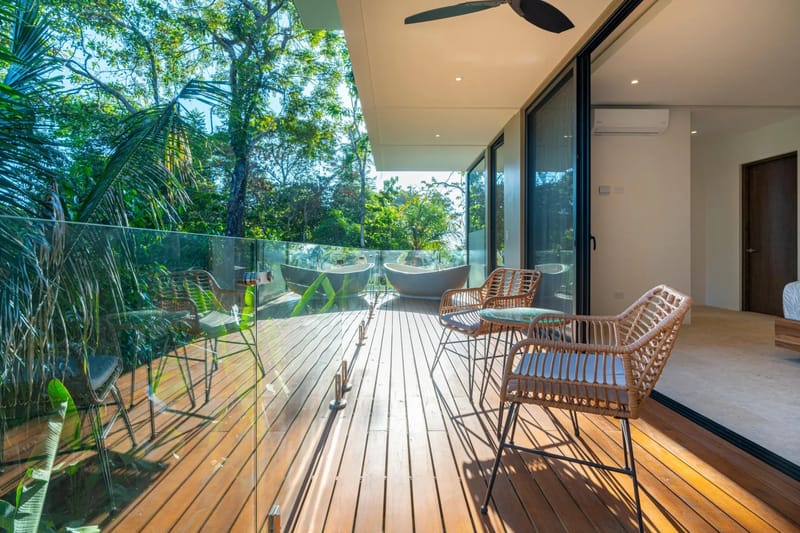 Colíbri Sur · 9. A private wooden terrace extends from a bedroom, featuring two outdoor bathtubs, a seating area with wicker chairs, and views of dense tropical jungle under natural light.