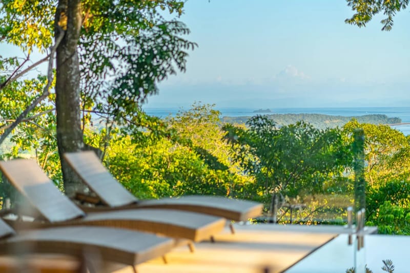 Colíbri Sur · 17. The sunlit pool deck with lounge chairs presents a wide view of the tropical forest and the sea stretching to the horizon.