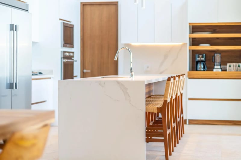 Colíbri Sur · 10. A bright, contemporary kitchen features a long island with an integrated sink and bar stools, alongside white cabinetry, built-in appliances, and open wood shelving.