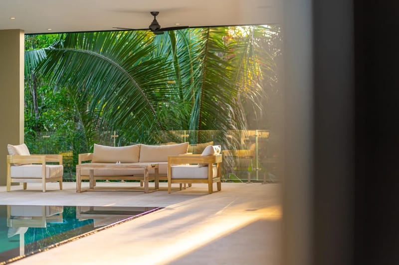 Colíbri Sur · 11. A covered terrace features a wood-framed outdoor seating area with light cushions, overlooking tropical foliage under natural sunlight, with a pool bordering the space.