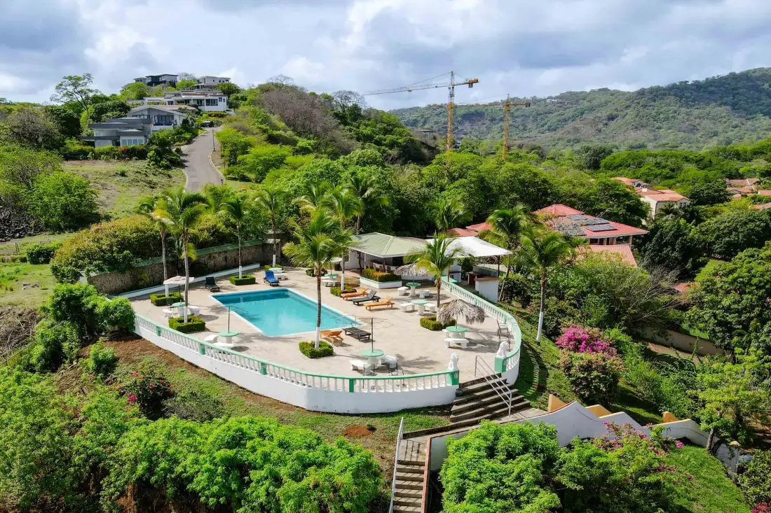 An outdoor swimming pool and surrounding seating sit amid lush hillside greenery.