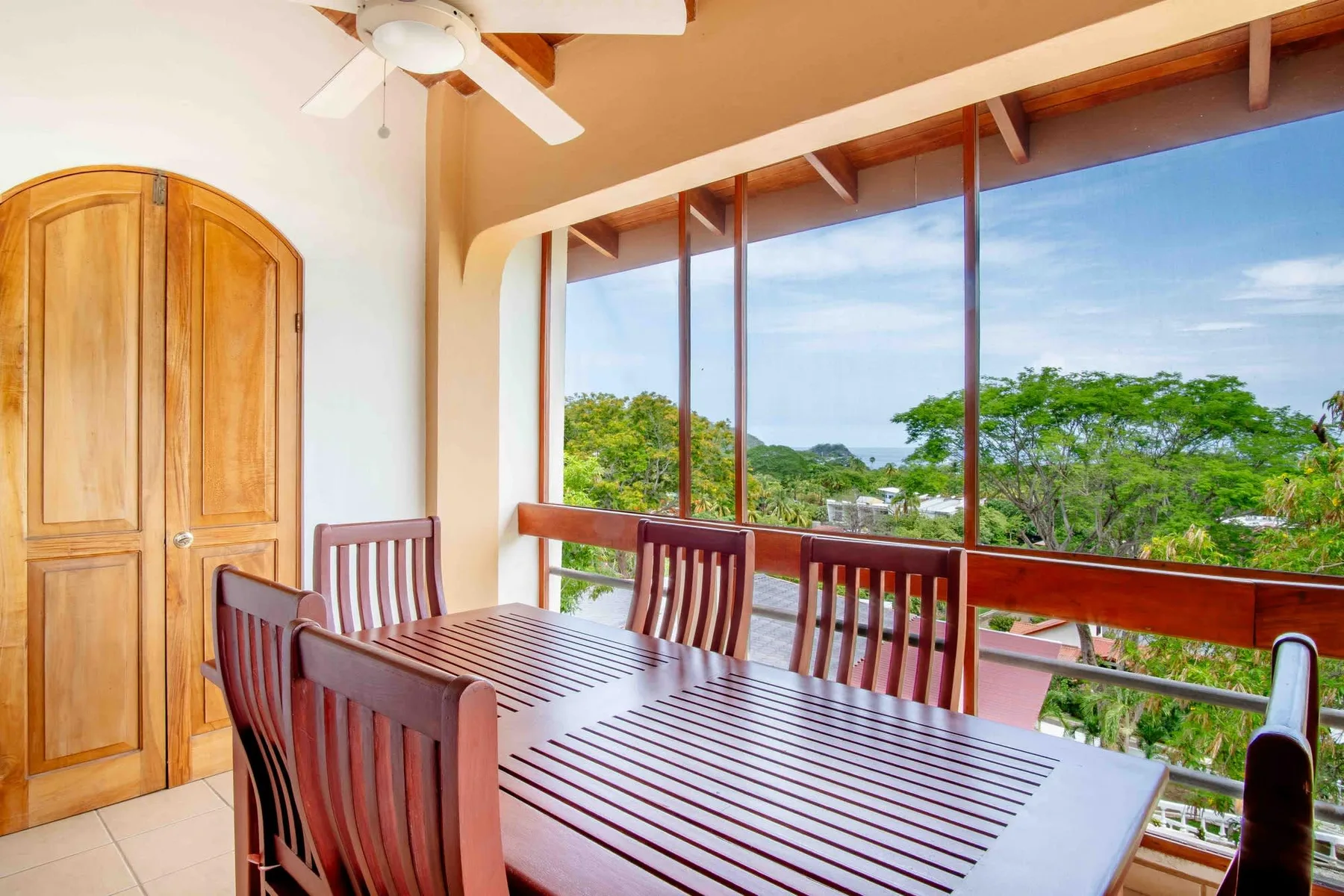 A dining area with a long table and a view of green trees through large windows.