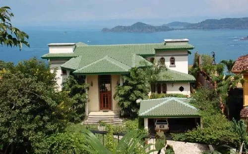 A green-roofed house sits among trees beside a bay.