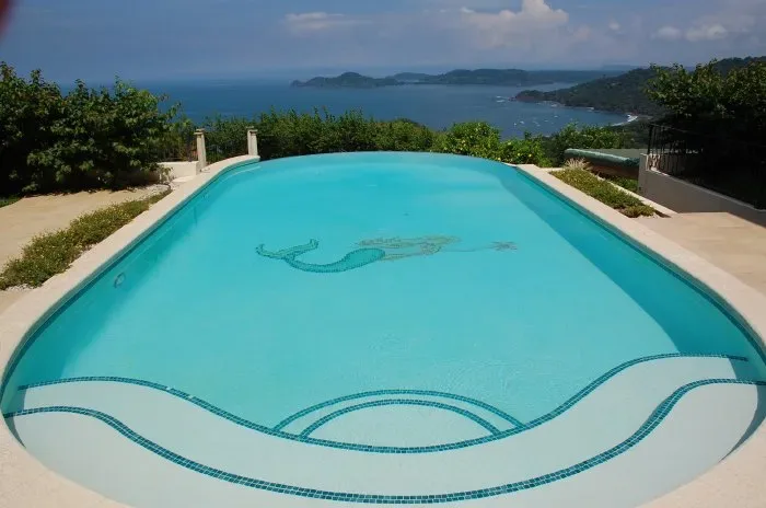 A swimming pool overlooks a blue bay and distant green islands.