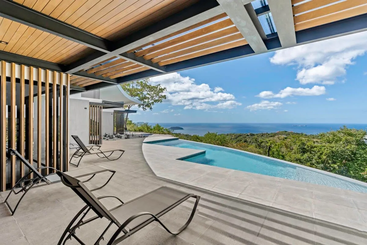 An outdoor pool terrace with lounge seating overlooks the sea.