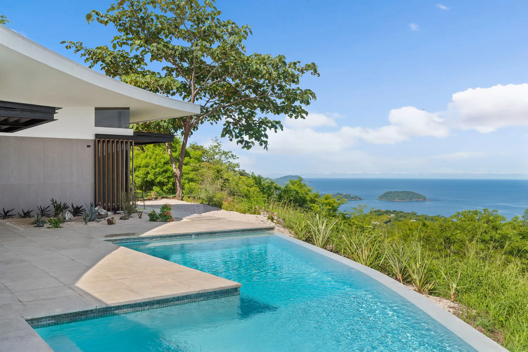An outdoor pool beside a modern house overlooks the ocean and a small island.