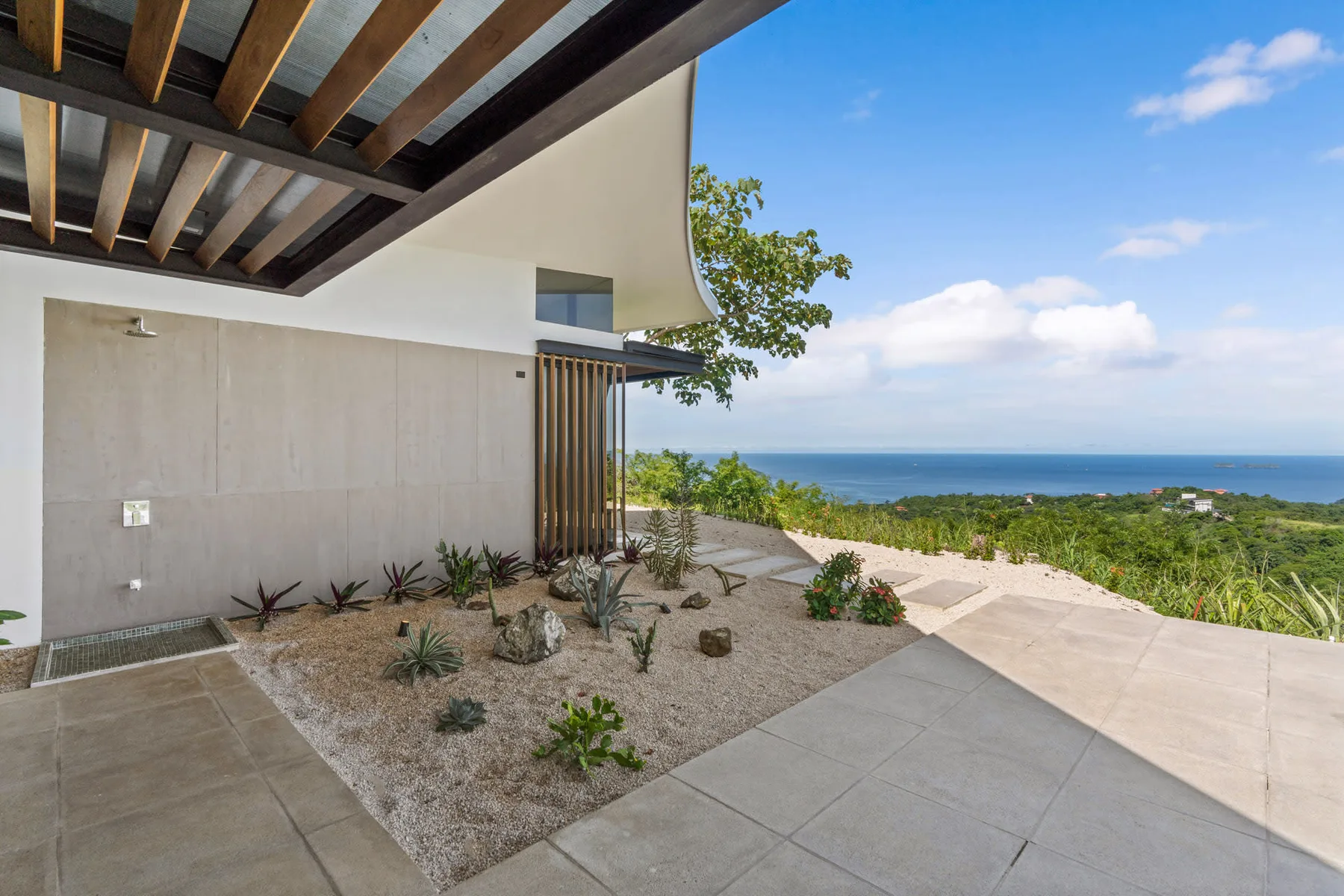 A modern house opens onto a tiled patio and a landscaped garden overlooking the sea.