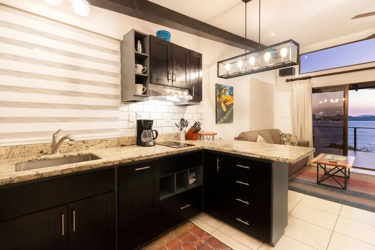A modern kitchen with dark cabinetry and a granite counter opens onto a seating area.