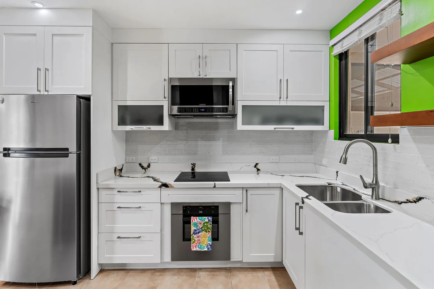 Una cocina blanca y luminosa con un refrigerador de acero inoxidable y una zona de cocción central.