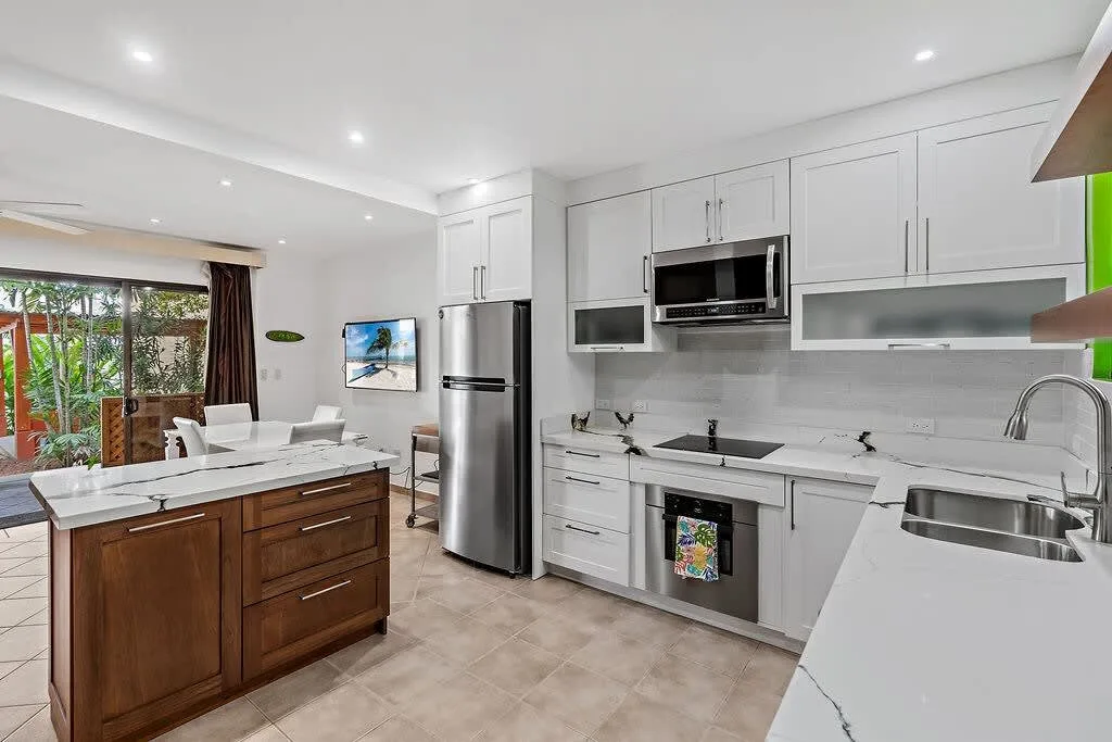 Una cocina luminosa con gabinetes blancos, electrodomésticos de acero inoxidable e isla de frente de madera.