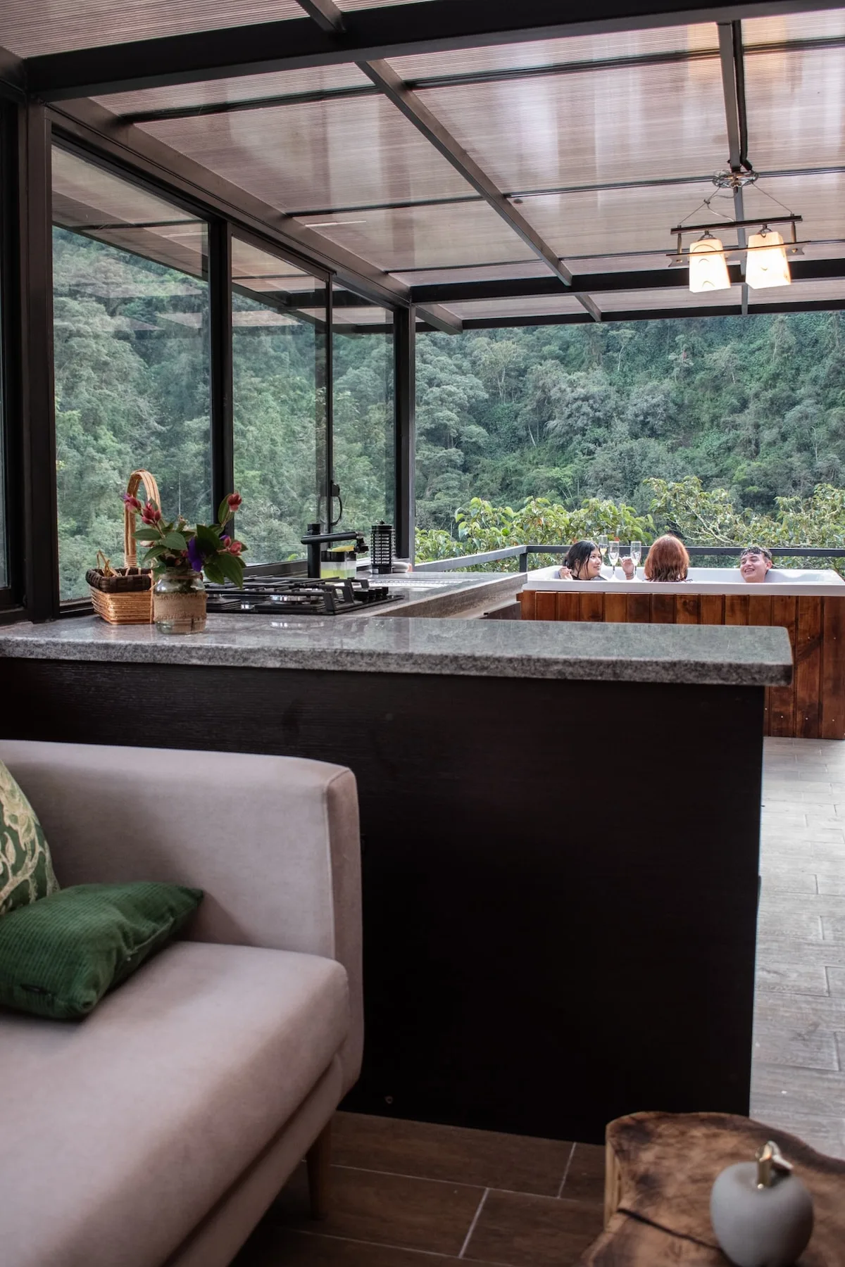 A modern kitchen opens onto a forested view, with a counter and seating area.