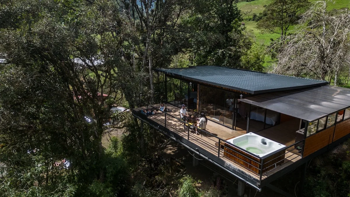 A raised wooden lodge with a deck and outdoor hot tub sits among trees.