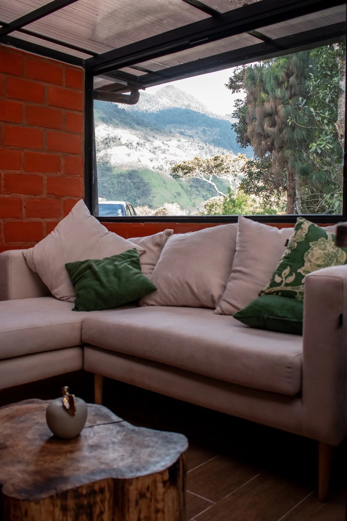 A living room seating area faces a large window overlooking a green mountain landscape.