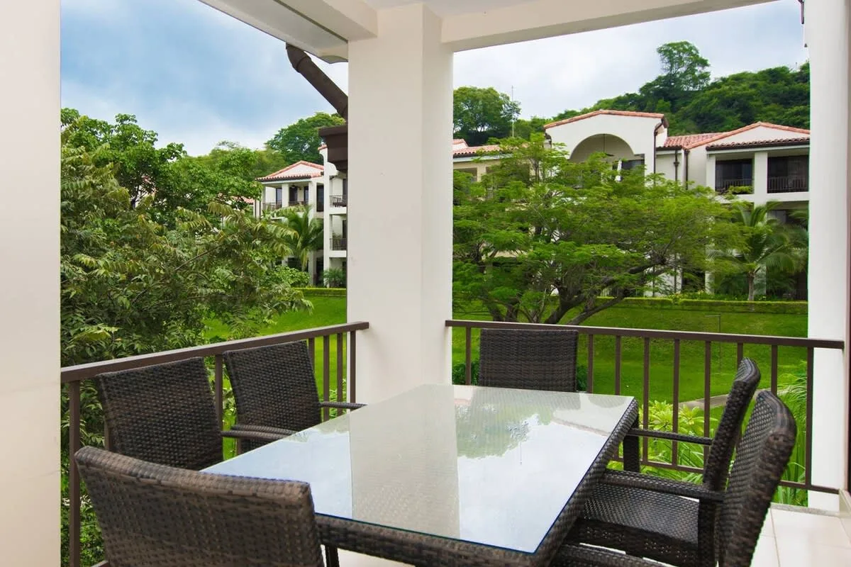 A covered outdoor dining area overlooks green gardens and nearby buildings.