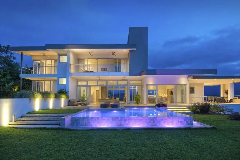 Una casa moderna al anochecer da a una piscina exterior iluminada.