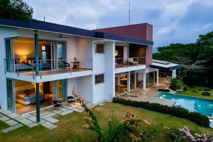 Una casa moderna de varios niveles se abre a balcones, un jardín y una piscina.