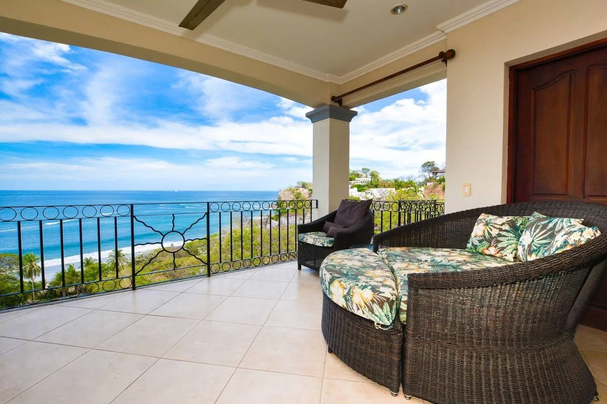 A covered patio with wicker seating overlooks the ocean.