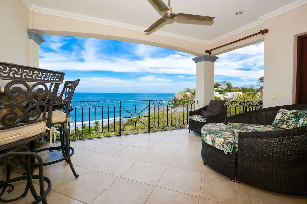 A covered seaside patio with dark seating and a view of the ocean.