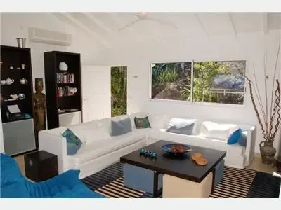 Una sala luminosa con asientos blancos, una mesa de centro oscura y vistas al jardín por las ventanas.