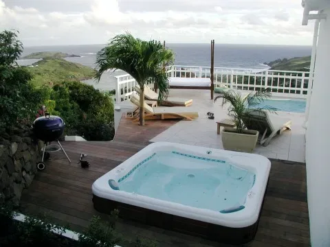 Una terraza al aire libre con jacuzzi, asientos y vistas al mar.