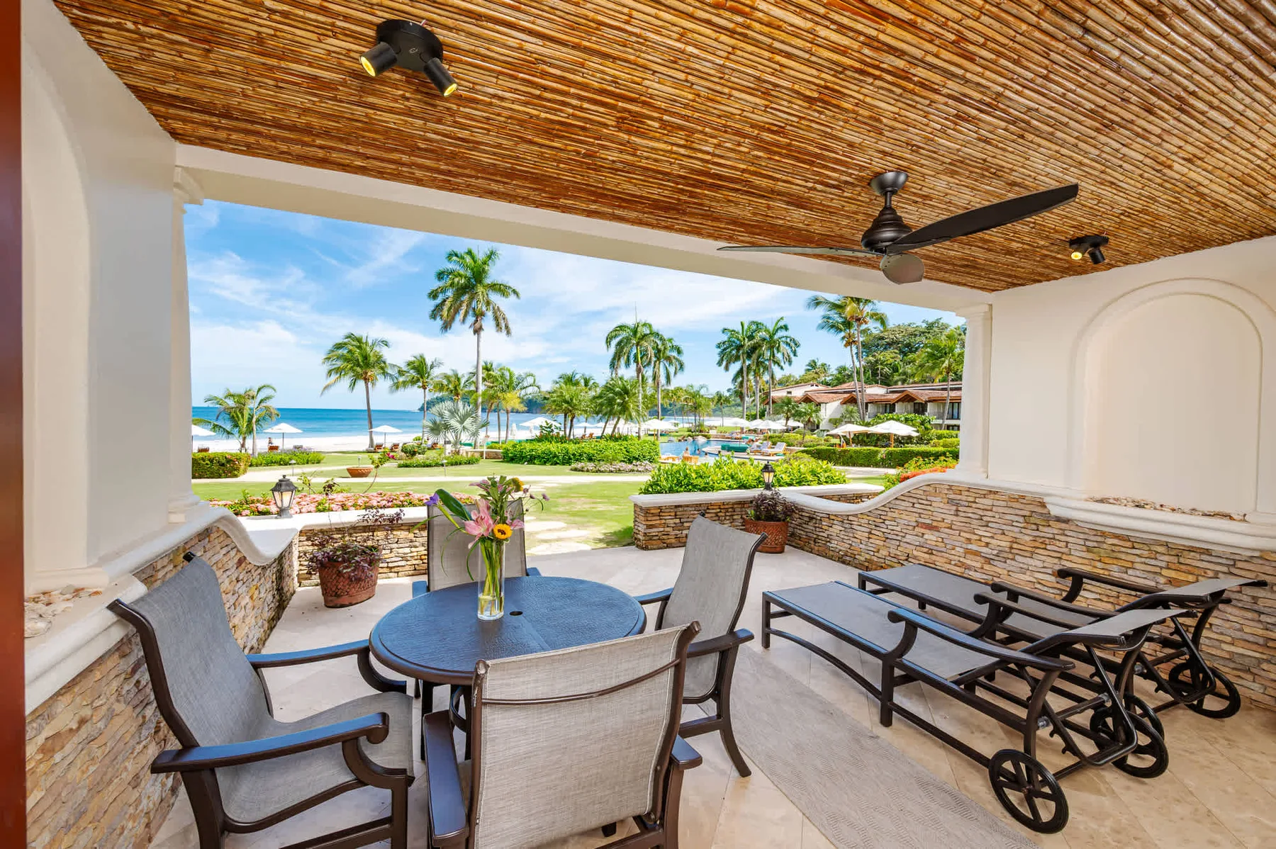 Un patio cubierto con asientos al aire libre da a un jardín junto a la playa.