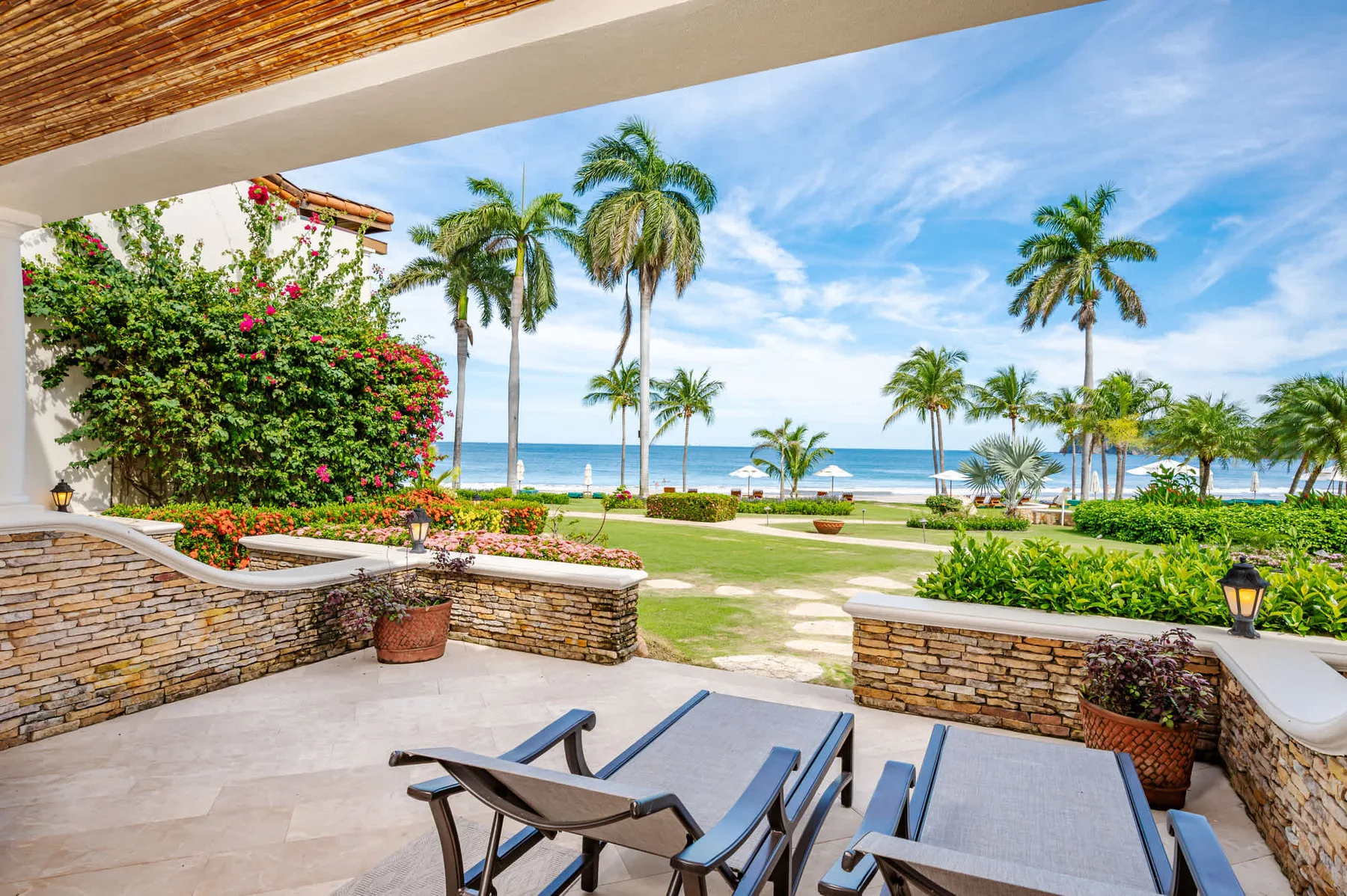 Un patio cubierto da a jardines, palmeras y el océano.