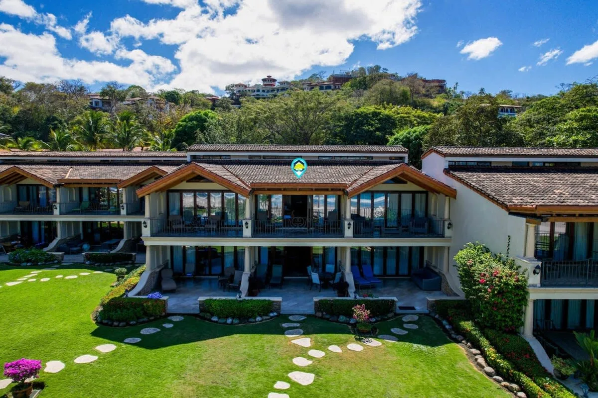 A multi-level building with balconies overlooks a green lawn and wooded hillside.