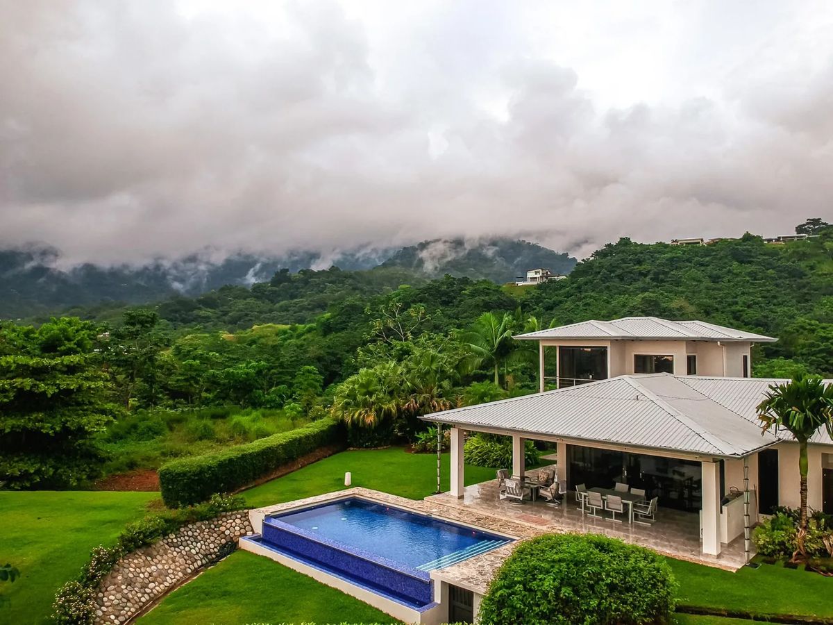 Casa Hacienda Jaguar · 6. A modern white villa features a blue tiled pool and covered outdoor dining area, all set against a backdrop of lush, mist-covered jungle mountains.