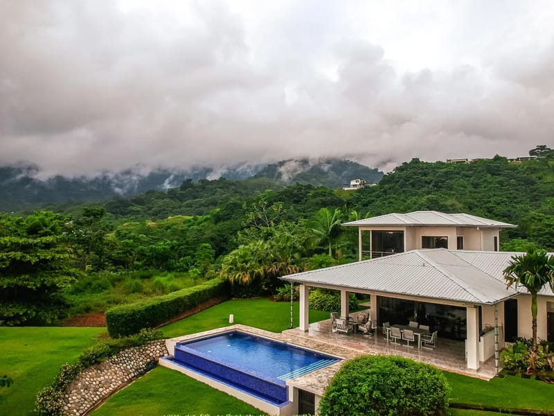 Casa Hacienda Jaguar · 6. A modern white villa features a blue tiled pool and covered outdoor dining area, all set against a backdrop of lush, mist-covered jungle mountains.