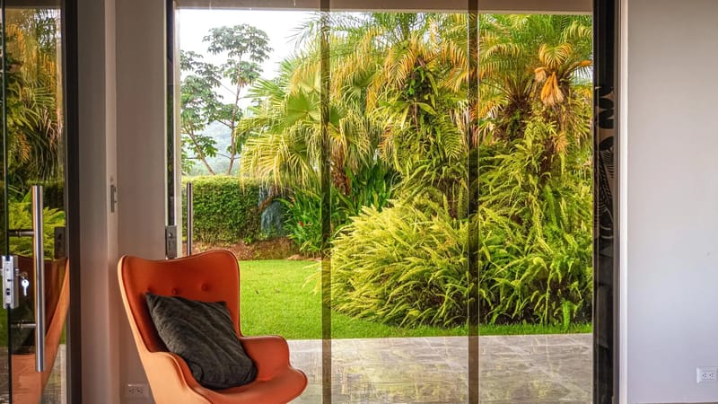 Casa Hacienda Jaguar · 22. The sunlit living area opens to a lush tropical jungle garden through expansive glass doors, connecting the interior with nature.