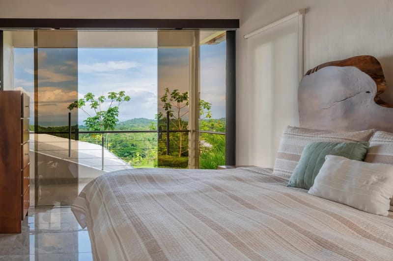 Casa Hacienda Jaguar · 29. This bedroom features a natural wood headboard and receives abundant light through full-height glass doors that open to a balcony with jungle and distant ocean views.